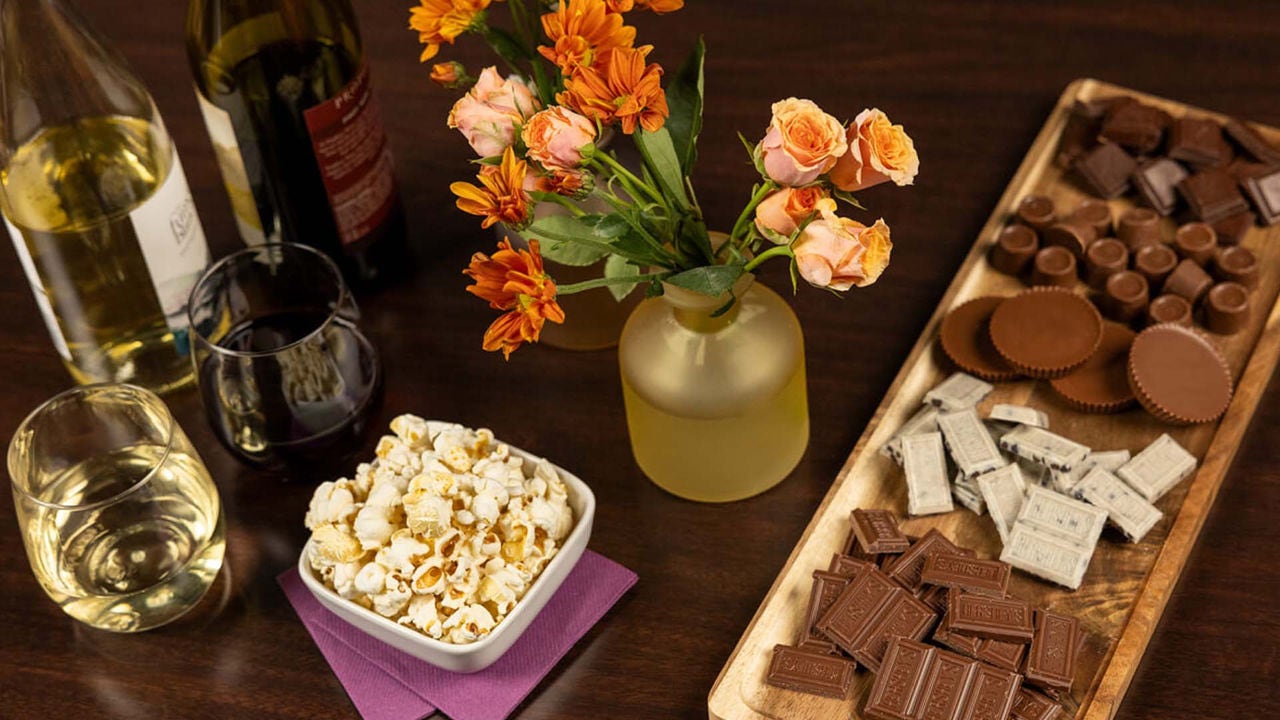 table filled with an assortment of unwrapped hersheys candies, wine, popcorn, and flowers