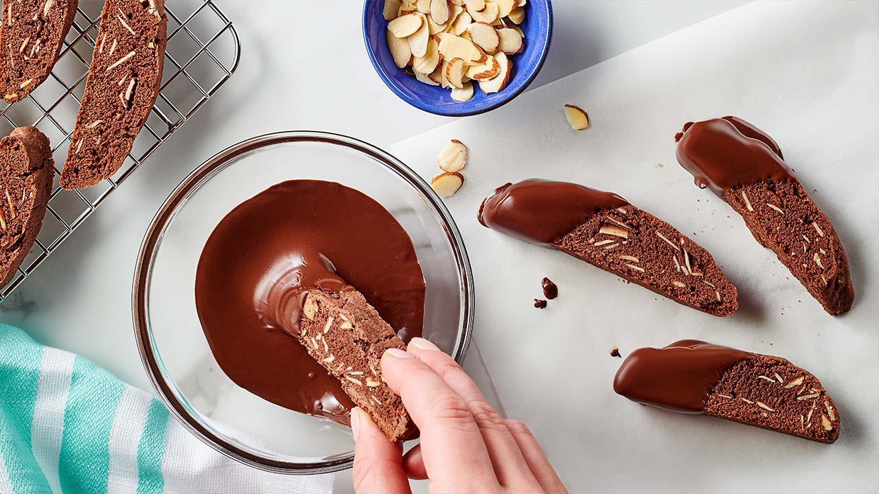 person dipping biscotti in chocolate glaze