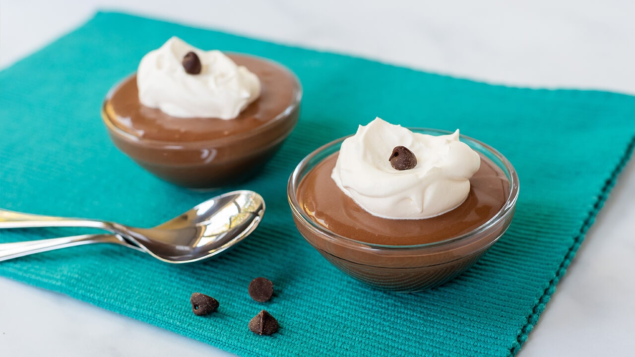 two bowls of chocolate protein pudding topped with whipped cream and a chocolate chip