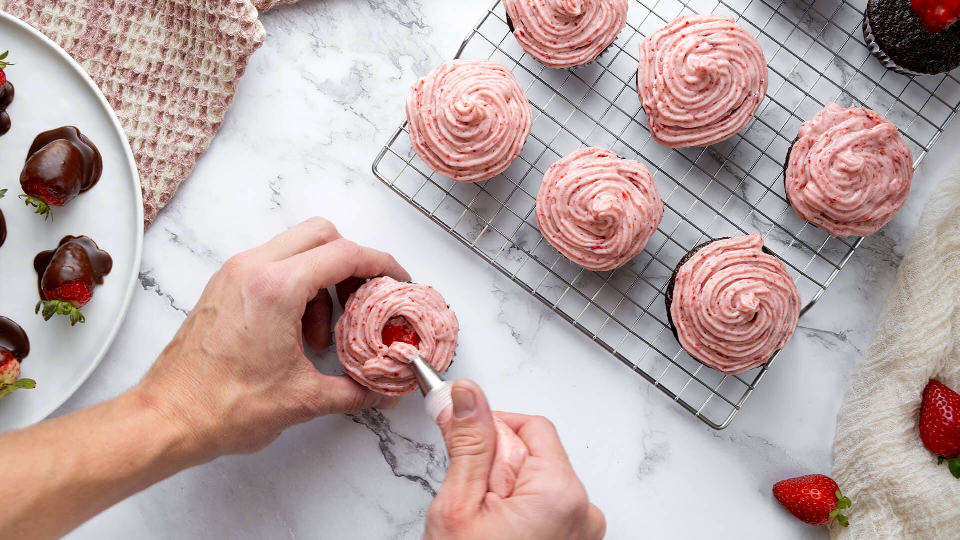 adding strawberry frosting to cupcakes