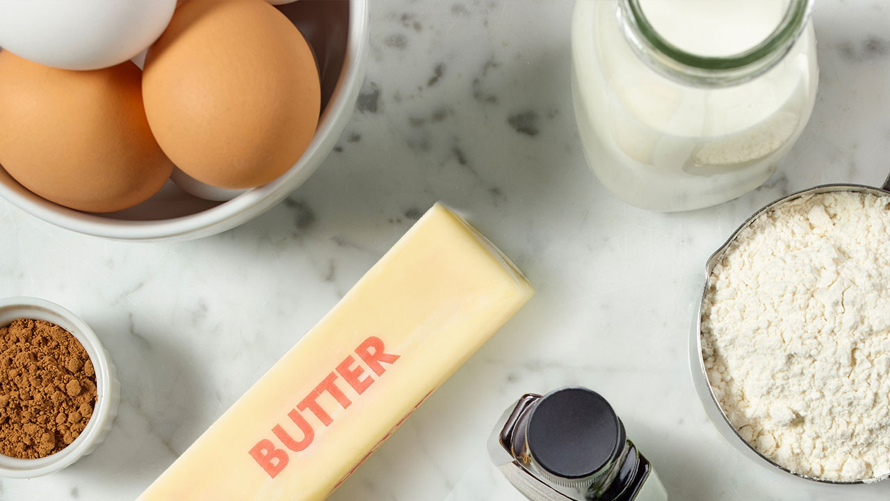 counter with eggs, flour, maple syrup, butter, milk, and cocoa powder