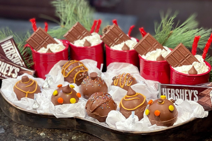 bowls filled tray of hot chocolate bombs in front of mugs of hot cocoa